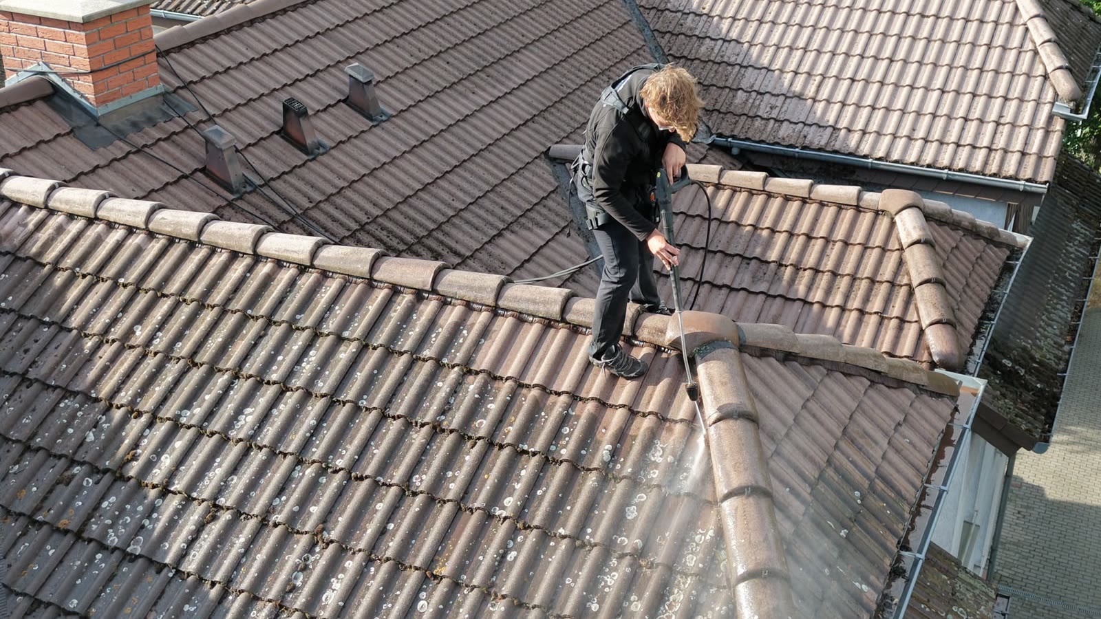 Blick von oben auf die Dachfläche während der Reinigung, der bearbeitete Streifen hebt sich vom bemoosten Bereich ab